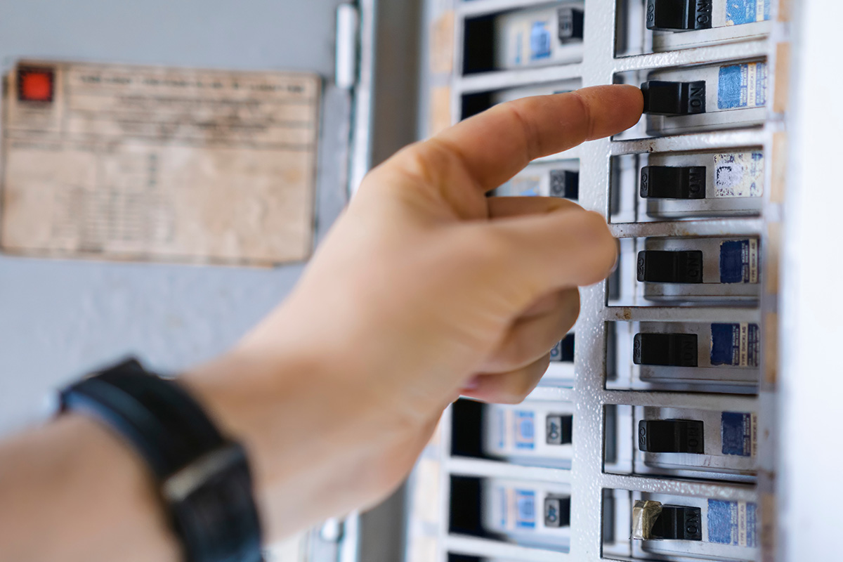 A Closeup Of A Hand Flipping A Switch On A Circuit Breaker.